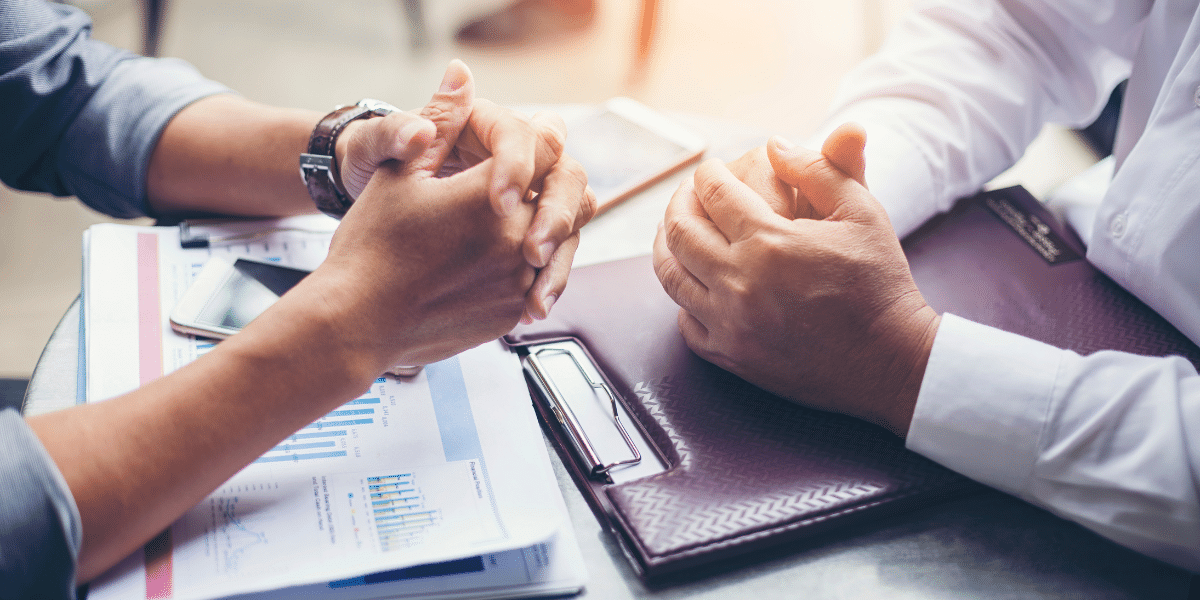 Two people in business attire discussing real estate documents with charts and a clipboard on a desk
