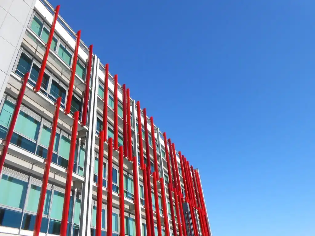 Wide shot of a sleek, modern manufacturing plant or factory exterior under a bright, sunny sky, representing industrial in...