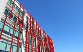 Wide shot of a sleek, modern manufacturing plant or factory exterior under a bright, sunny sky, representing industrial in...